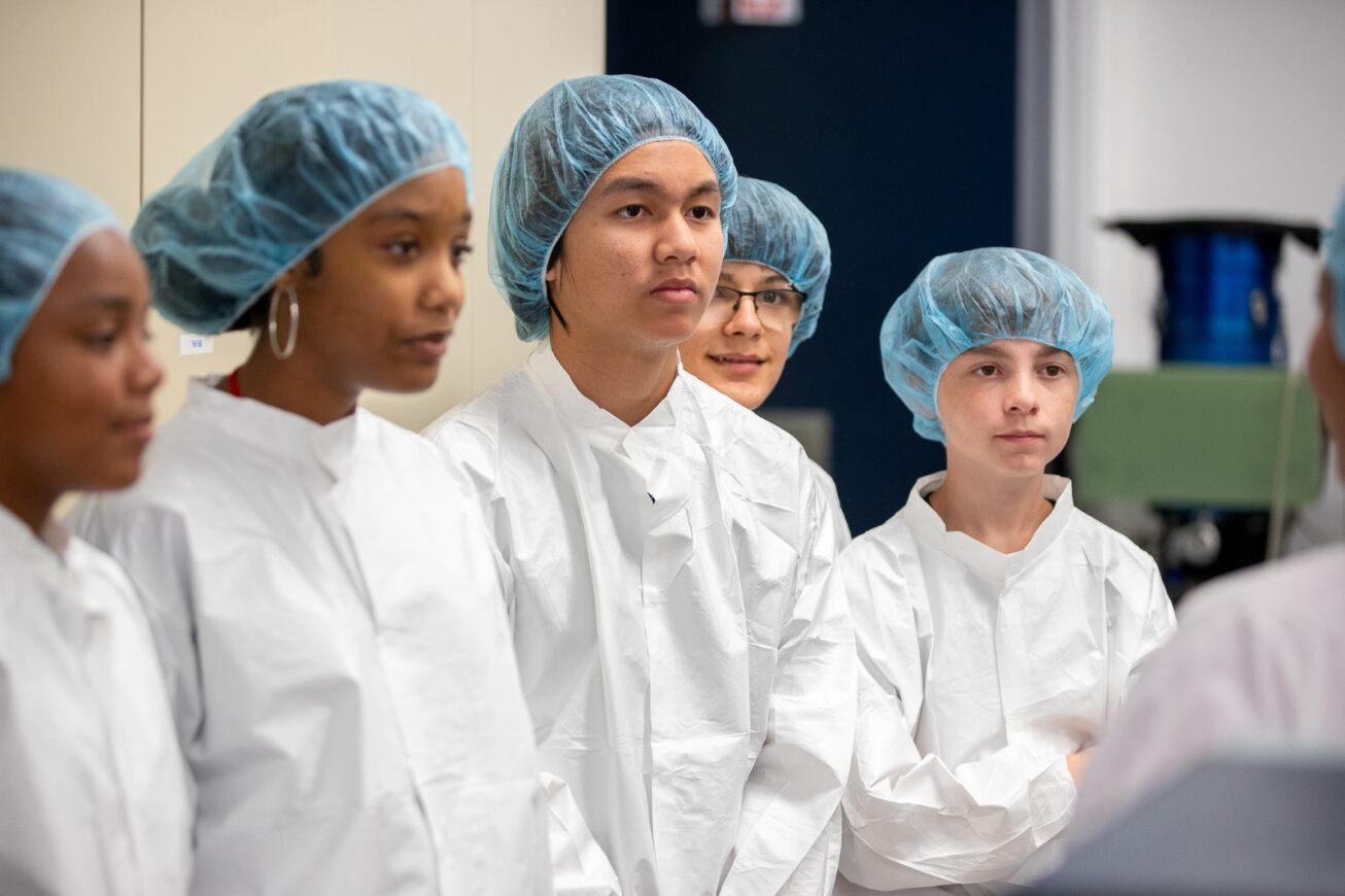A group of students wearing white lab coats and blue hair nets