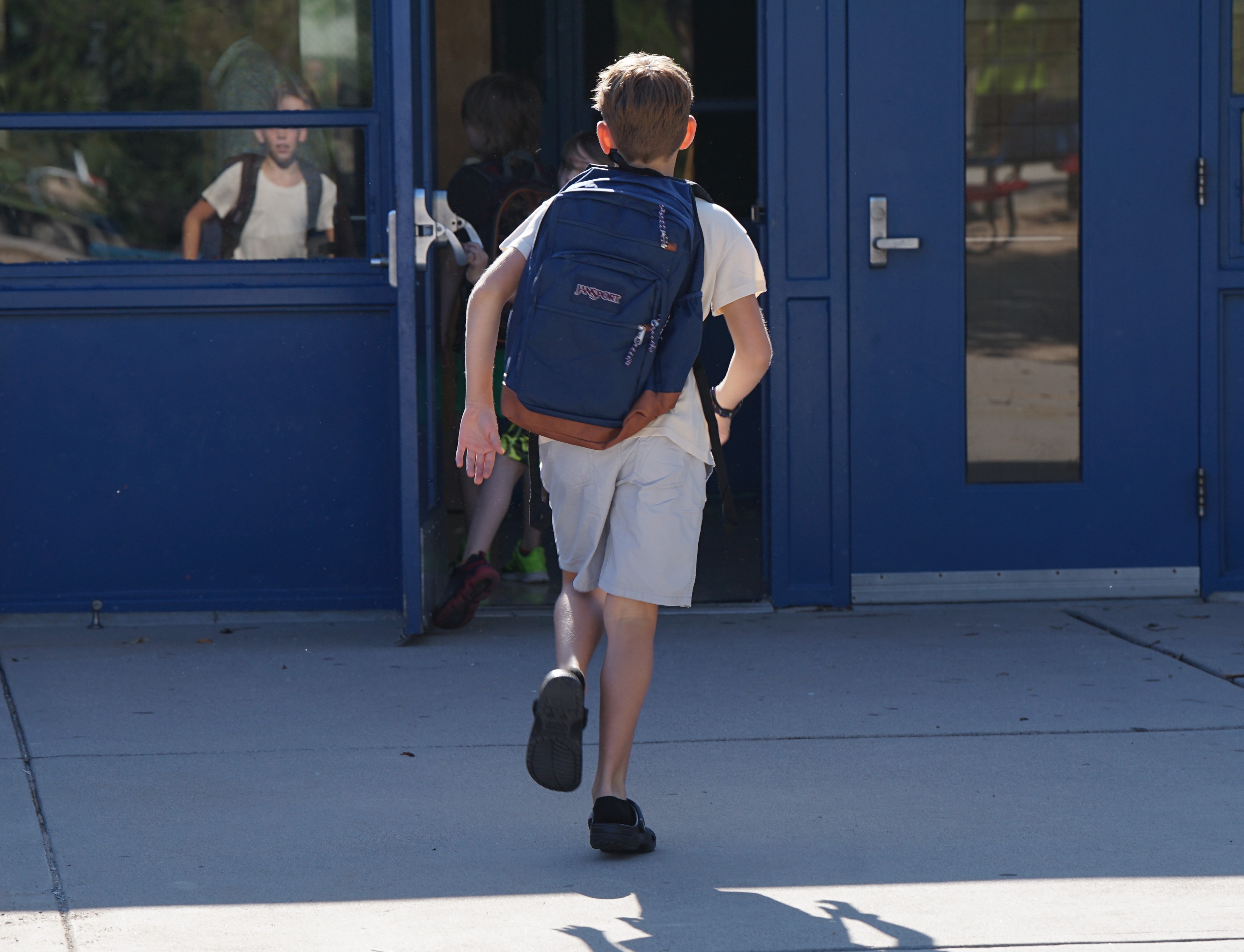 A boy runs into school with his blue backpack on