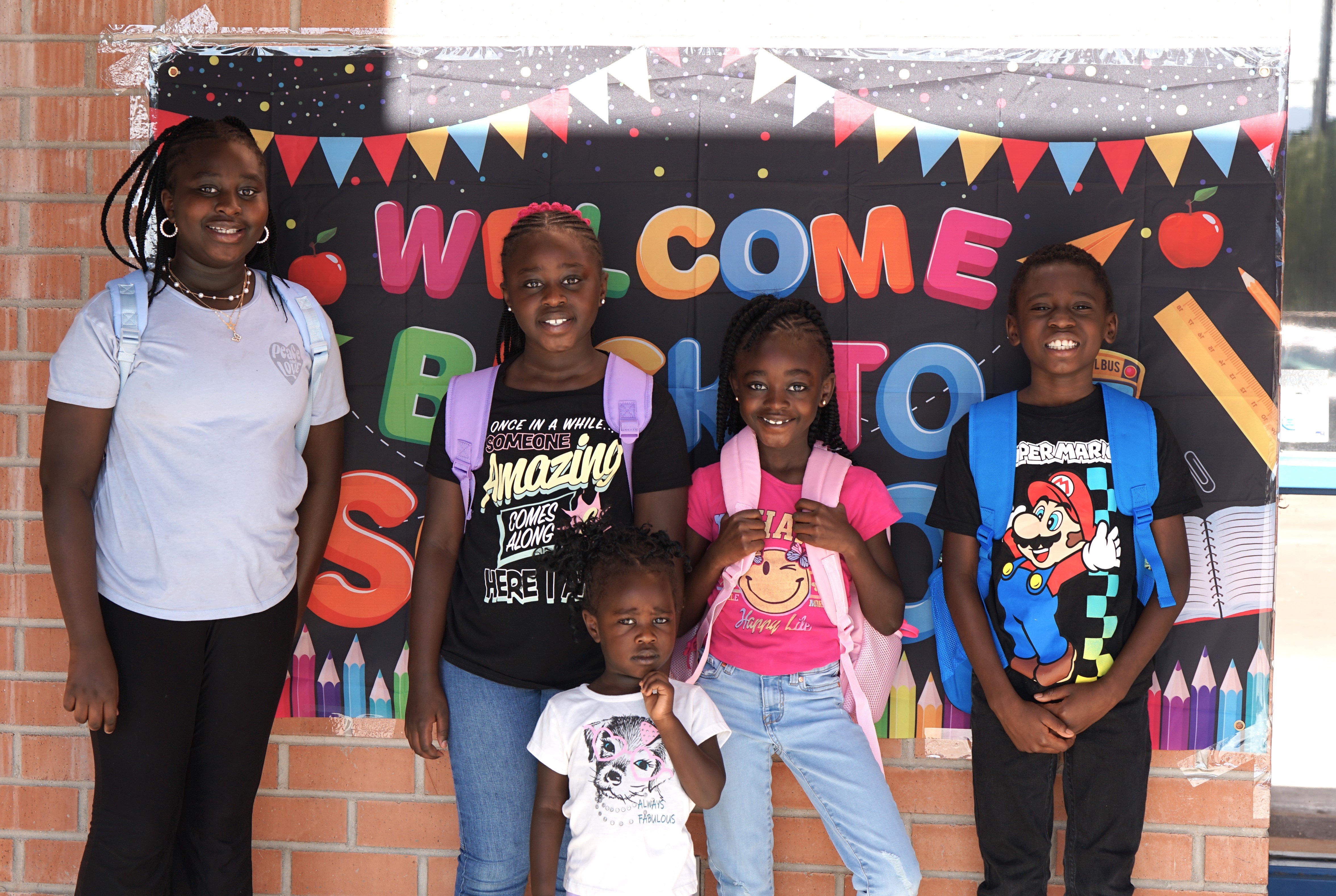 Five students smile big in front of a Welcome Back to School banner