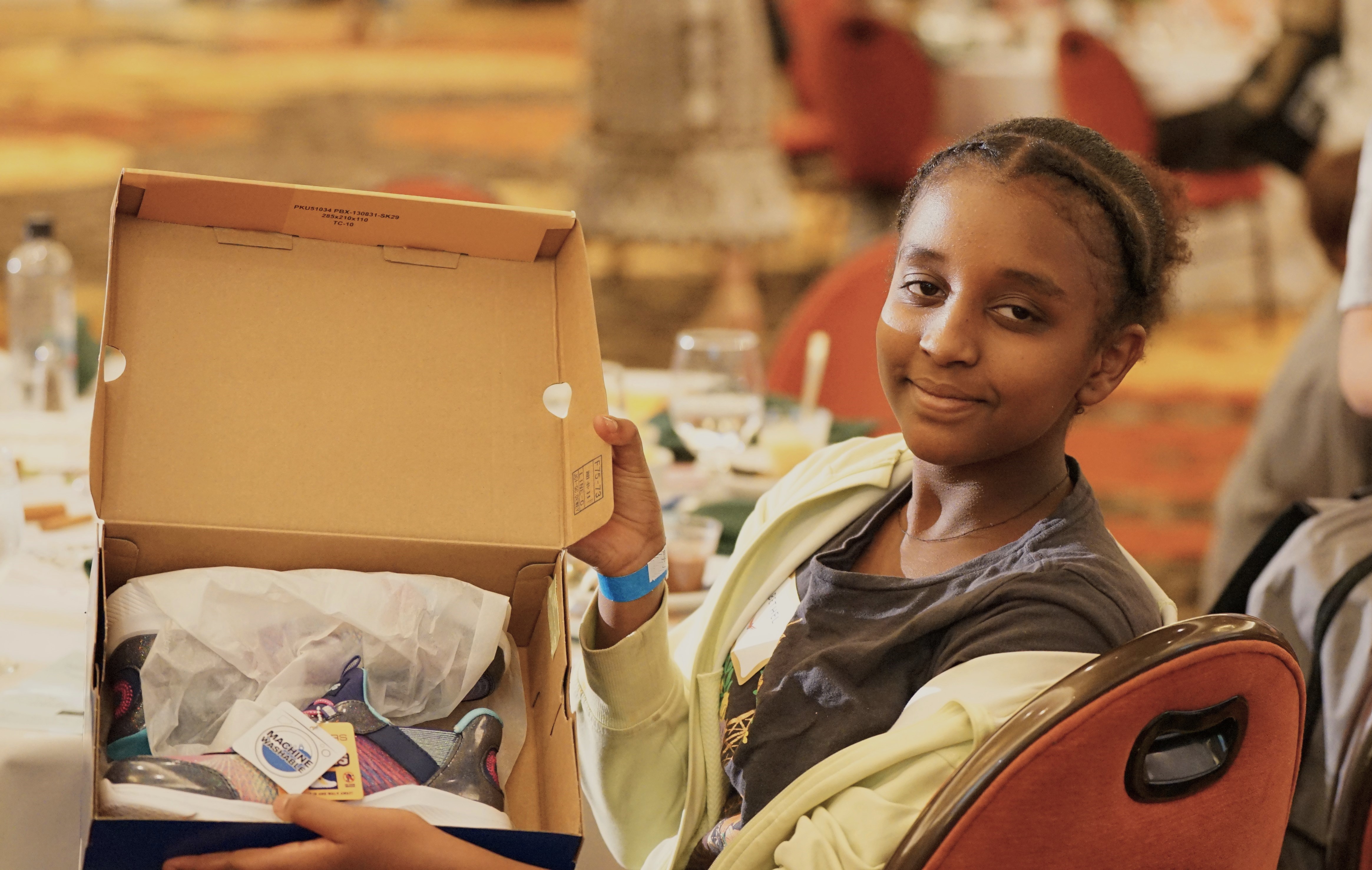 A girl smiles and holds up her new pair of shoes in their box