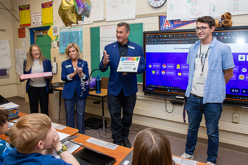 A man in a blue suit jacket holds up a certificate as he talks about the man, right, in glasses and a blue shirt