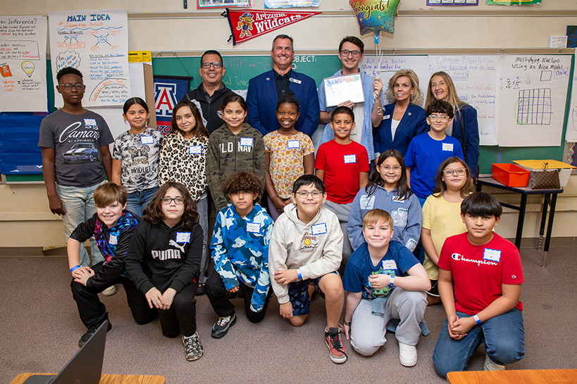 A classroom of students, their teacher, and reps from the Arizona Bowl pose for a group photo