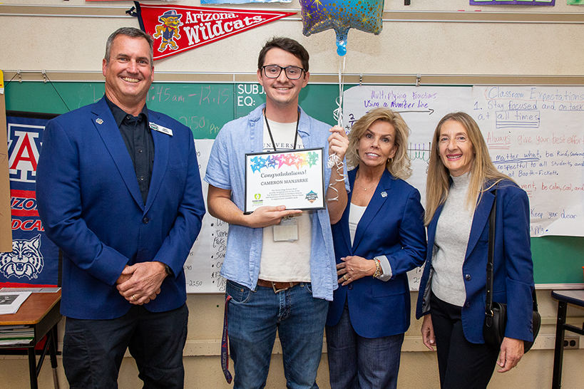 From left to right, a man in a blue suit jacket, a man in a blue button down holding a certificate and balloon, two women in blue suit jackets