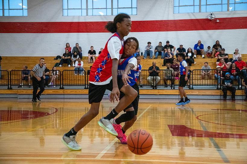 A boy in a red jersey tries to get the basketball away from a boy in a blue jersey