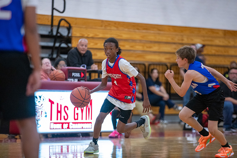 A boy in a red jersey dribbles the basketball down the court