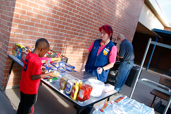 A little boy puts condiments on  his hot dog