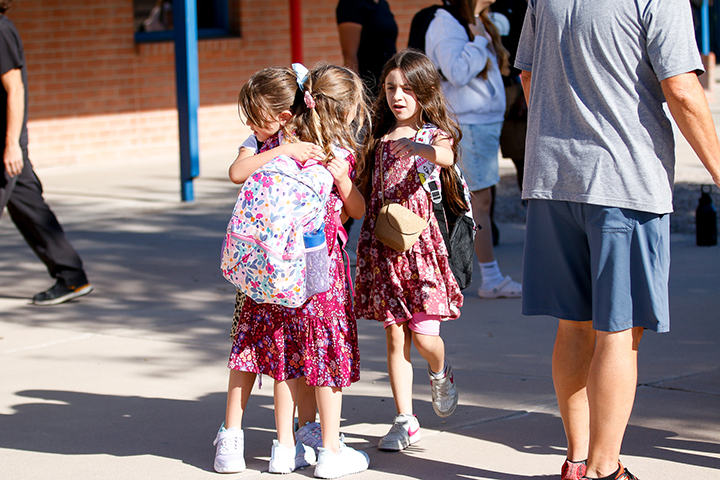 Three young girls in floral dresses hug each other