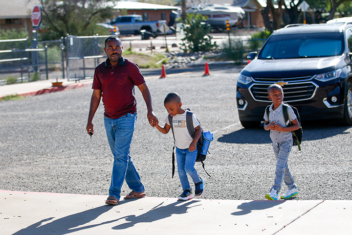 A dad leads his two young sons from the parking lot