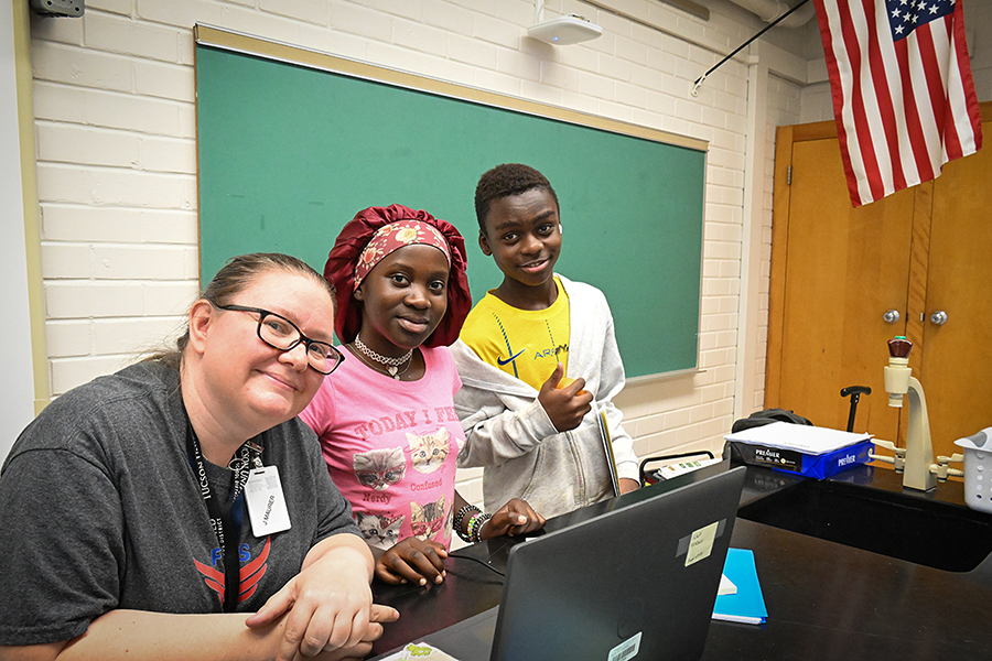 A woman in glasses poses with two of her new students