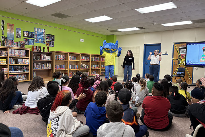 A person dressed up as a blue cat reads to students in the library