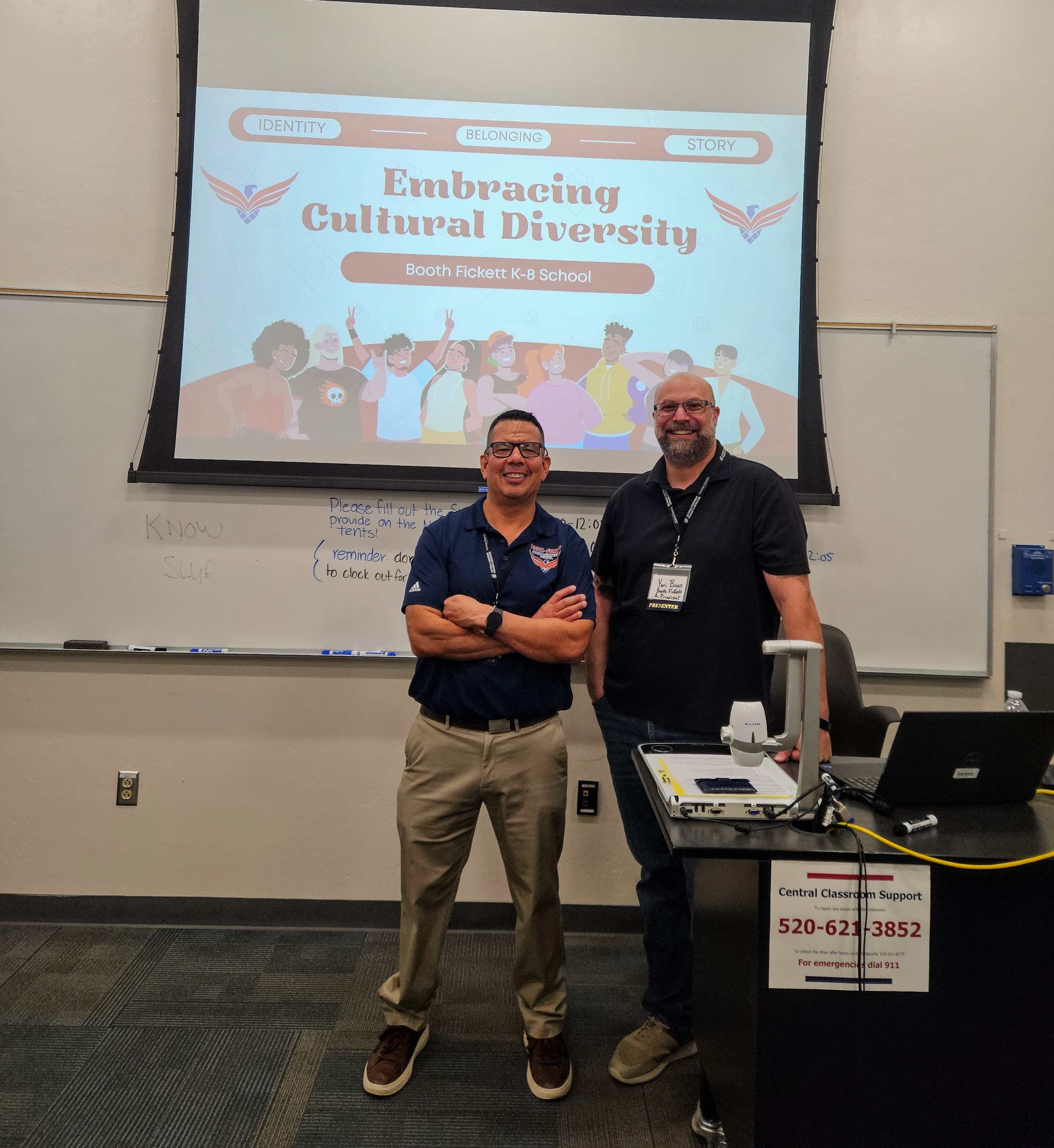 Two men stand in front of a screen with a presentation about Embracing Cultural Diversity