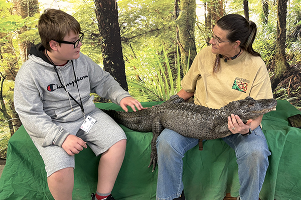 A woman holds an alligator while a preteen boy pets it
