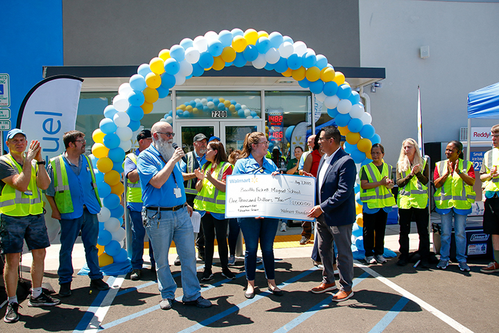 A woman gives a man a giant check under a blue, yellow and white balloon arch