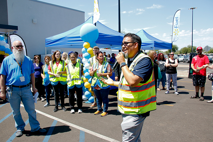A man in a yellow safety vest talks in a microphone to a crowd