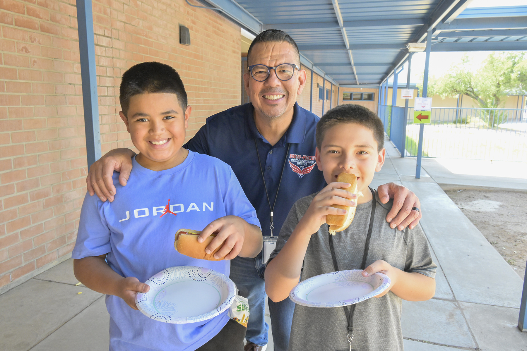 The principal, center, smiles with two of his students as they enjoy their hot dogs